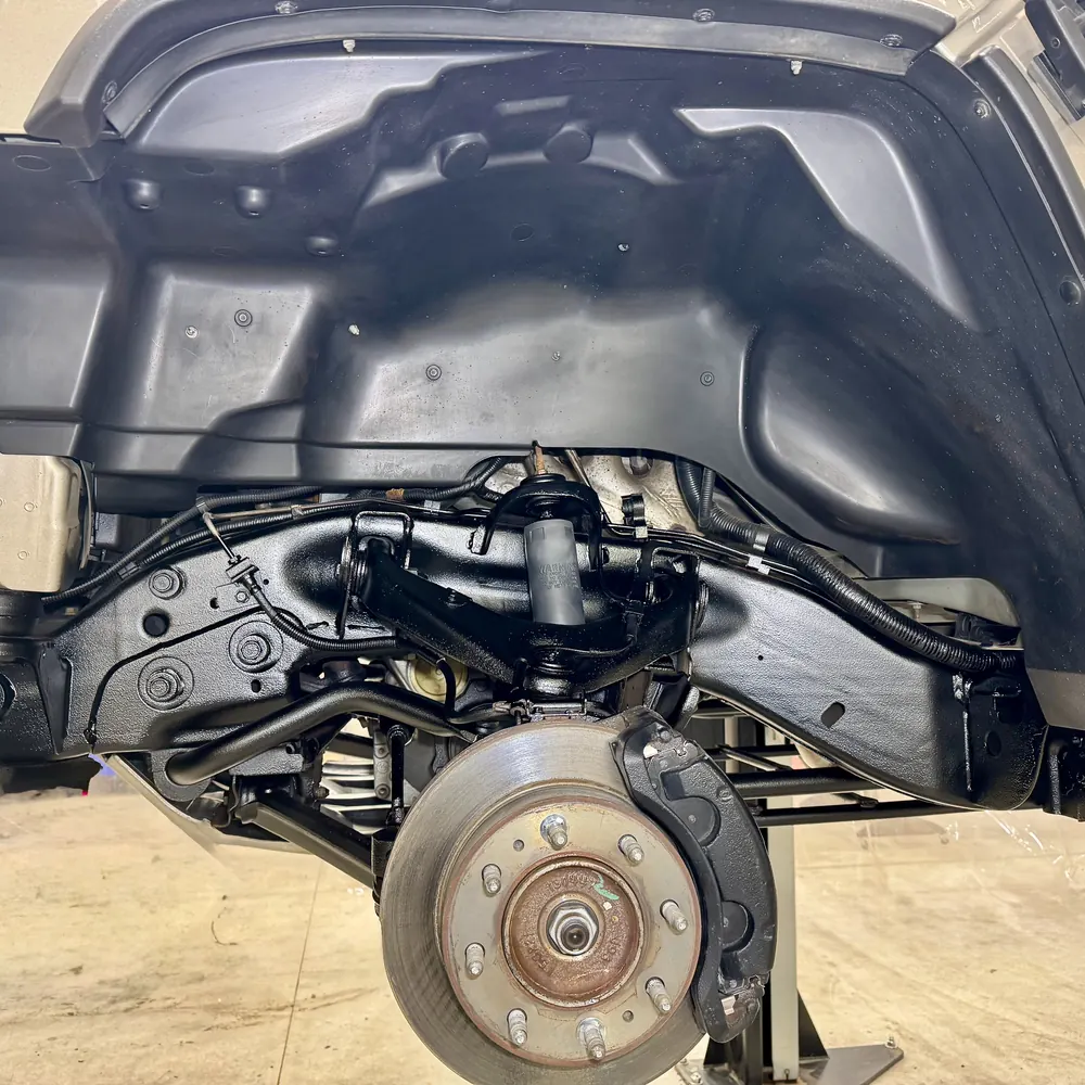 The same front wheel well after undercoating, frame rail and control arms sealed in black DINITROL 4941