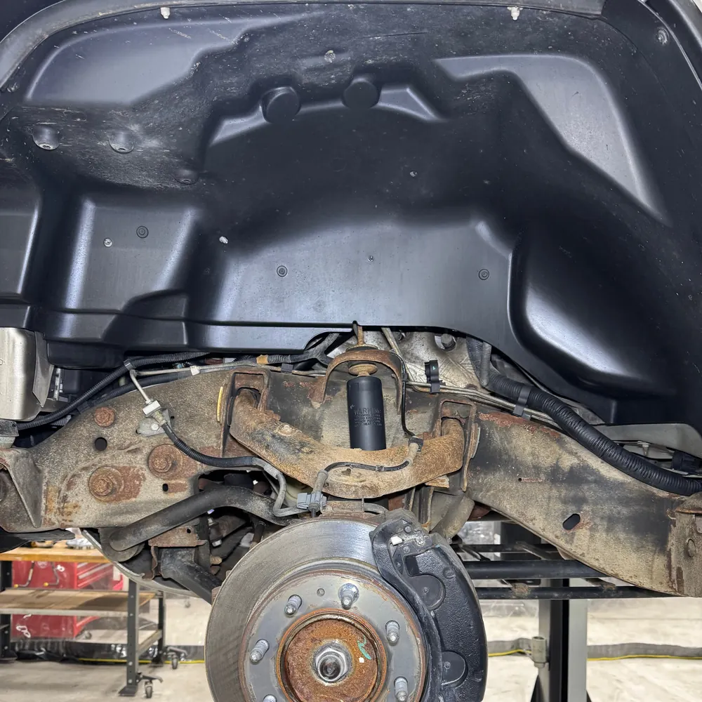 Hummer H2 front wheel well before cleaning, with rust-scaled frame rail and control arm
