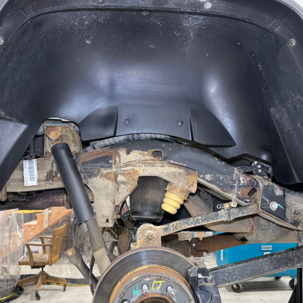 Hummer H2 rear wheel well before cleaning, with rust scale and road grime on the frame rail, trailing arm and shock mount
